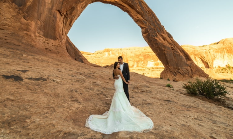 bride and groom pose under a red rock natural arch